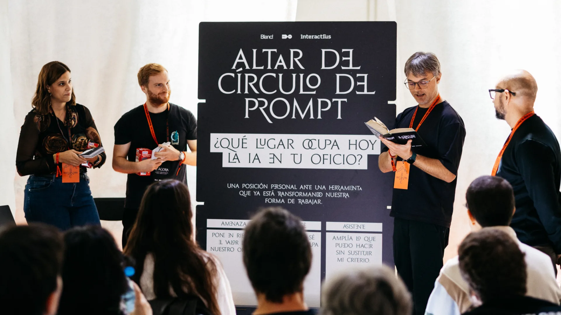 Plafó de l'Altar del Cercle del Prompt amb la pregunta «Quin lloc ocupa avui la IA en el teu ofici?» i les tres opcions a sota: amenaça, no ho sé i assistent. Quatre persones dretes a banda i banda, una d'elles llegint d'un llibre, i el públic assegut d'esquena.