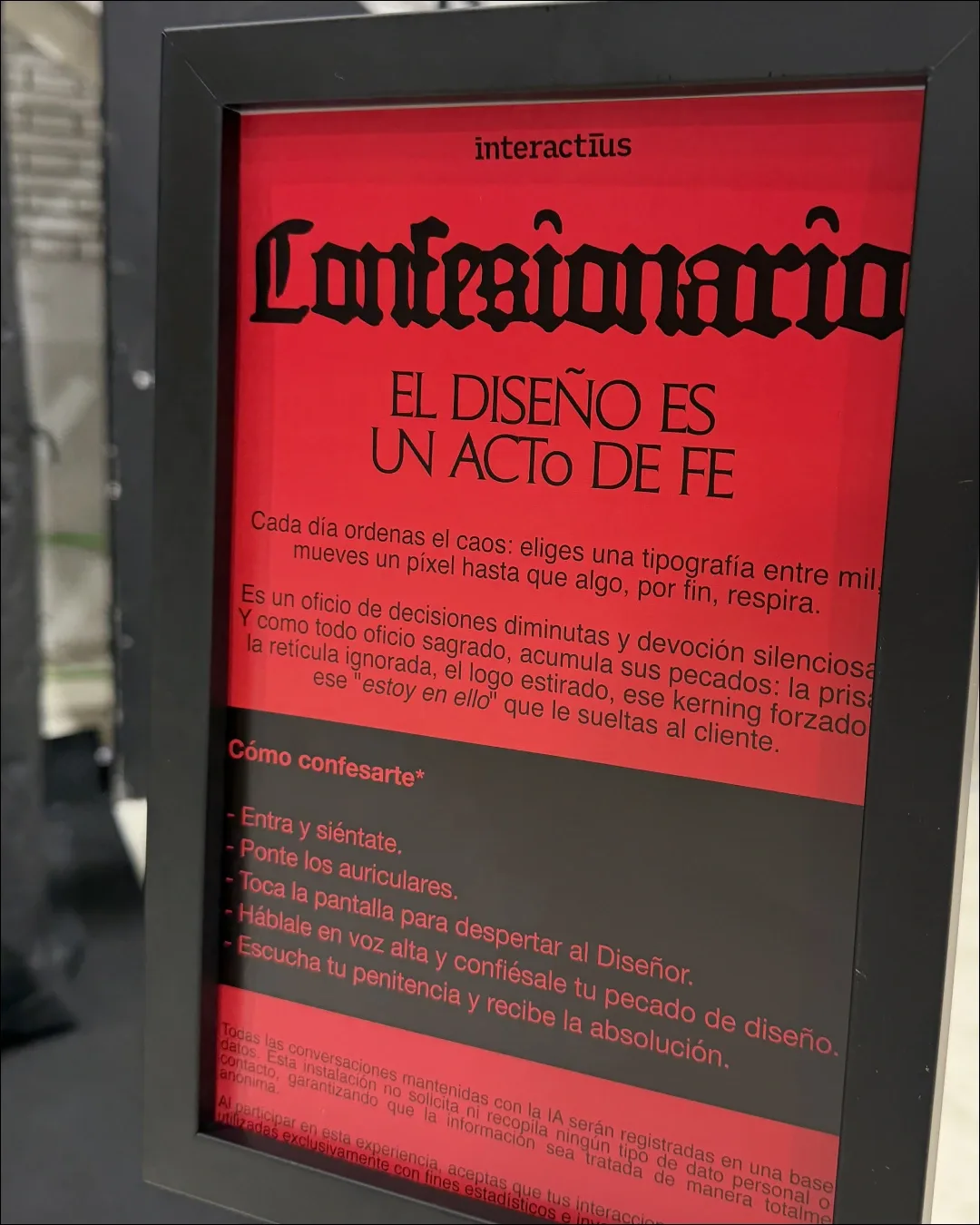 Cartell emmarcat del Confessionari sobre fons vermell, amb el títol en lletra gòtica i el lema «El disseny és un acte de fe», seguit de les instruccions per confessar-se.